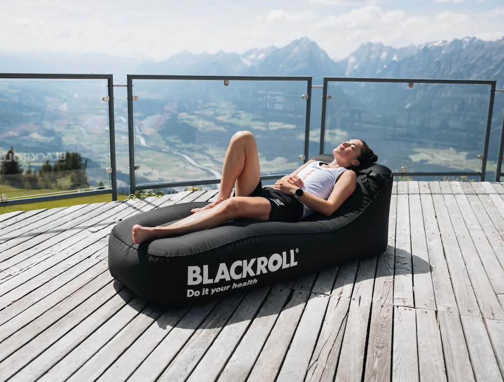Person relaxing on BLACKROLL Inflatable Lounger outdoors after training session